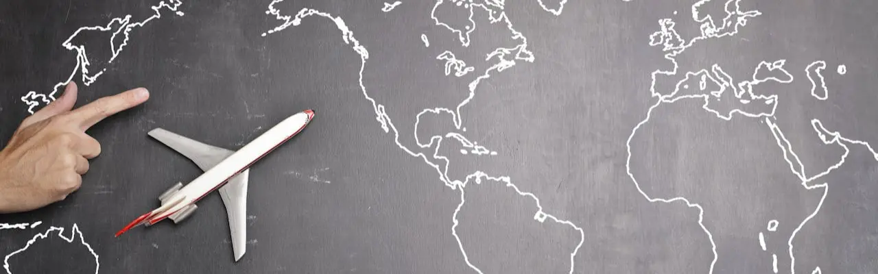 one hand points to a world map, there is a toy airplane and several countries can be seen.